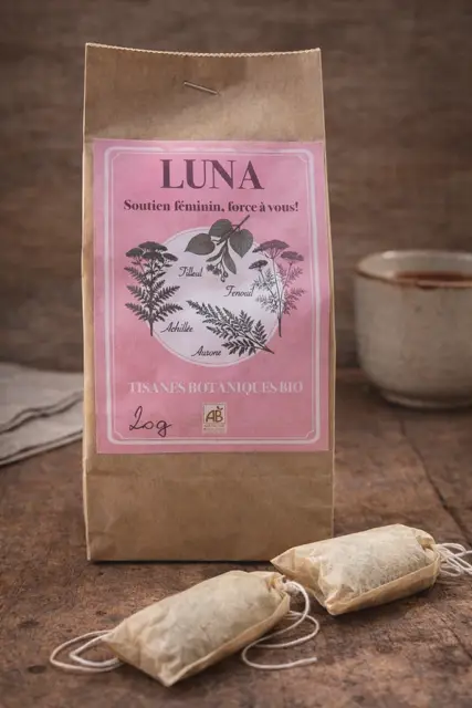 Sachet kraft de tisane botanique bio Luna, avec étiquette rose illustrée de plantes et sachets d’infusion sur une table en bois.